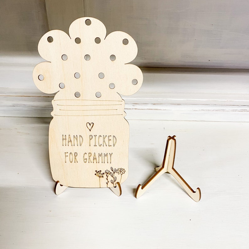 May include: Wooden cutout of a mason jar with a flower top, with the text "HAND PICKED FOR GRAMMY" and a small heart. The cutout is on a wooden stand.