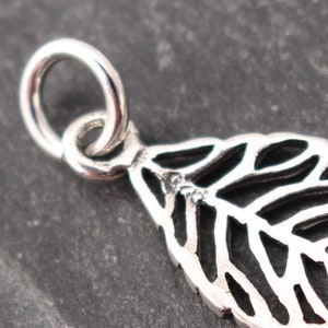 Op de afbeelding: Close-up van een zilveren blad hanger met ingewikkelde openwerk details. De hanger heeft een kleine lus om aan een ketting te bevestigen. Het bladeren ontwerp is gedetailleerd en delicaat, met een gepolijste afwerking.
