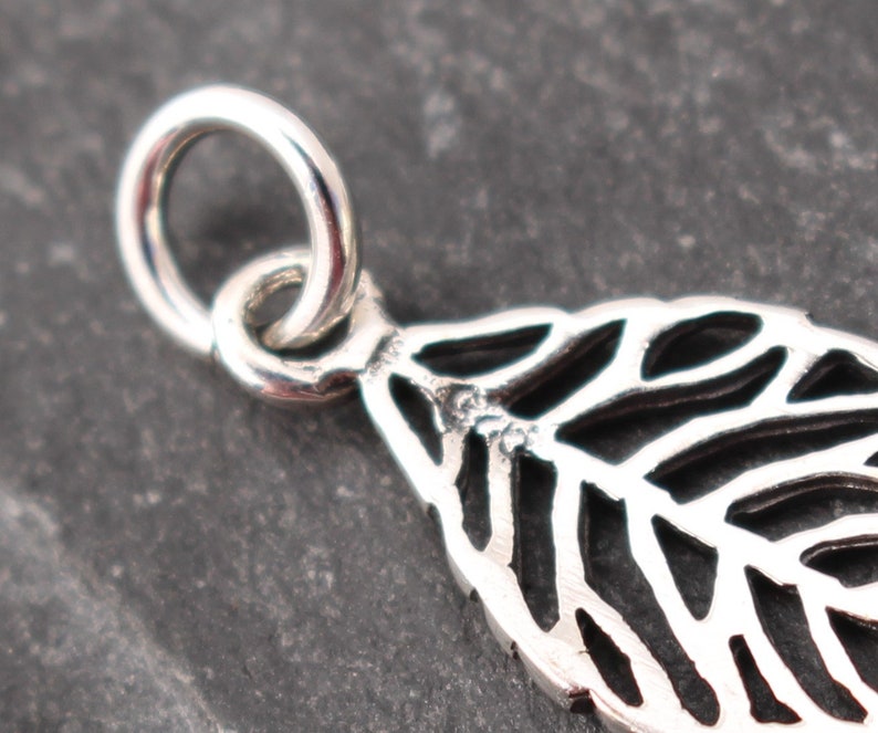Op de afbeelding: Close-up van een zilveren blad hanger met ingewikkelde openwerk details. De hanger heeft een kleine lus om aan een ketting te bevestigen. Het bladeren ontwerp is gedetailleerd en delicaat, met een gepolijste afwerking.