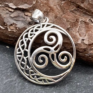 May include: A silver pendant featuring a Celtic knot design. The pendant has a circular shape with intricate knotwork around the edge and a central triskele symbol. The pendant is made of shiny metal and has a small loop at the top for a chain.