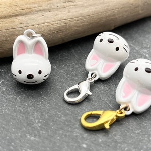 May include: White bunny charm with pink inner ears and black facial details. Two charms have silver clasps, and one has a gold clasp. The charms are likely for jewelry or crafts.