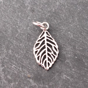 Op de afbeelding: Een zilverkleurige bladbedel met een gedetailleerd, opengewerkt ontwerp. De bedel is bevestigd aan een kleine ring, klaar om aan een ketting of armband te worden toegevoegd. De bladvorm is een klassiek, door de natuur ge&iuml;nspireerd element.