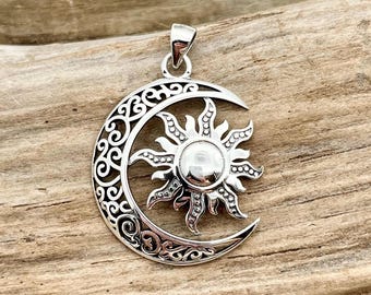 May include: A silver pendant featuring a sun and moon design. The sun is in the center, with rays extending outward. The moon is a crescent shape, with an ornate, swirling pattern. The pendant has a loop for a chain.