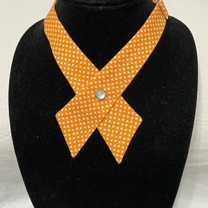 May include: Orange and white polka dot fabric necktie with a white button. The tie is on a black mannequin.