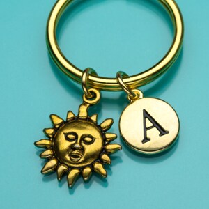 Peut inclure: Porte-clés en or avec un charme soleil et un charme lettre A. Le charme soleil a un visage et le charme lettre A est noir sur or.