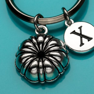 May include: Silver keychain with a flower charm and a round charm with the letter X on it. The charms are attached to a silver key ring.