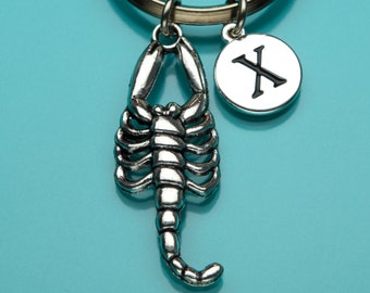 Puede incluir: Llavero de plata con un dije de escorpión y un dije de plata con la letra X. Los dijes están unidos a un anillo de plata.