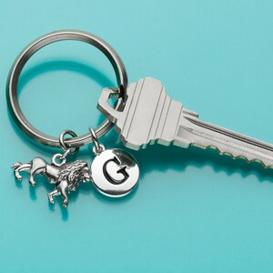 May include: A silver key chain with a lion charm, a silver charm with the letter G, and a silver key. The keychain is on a blue background.
