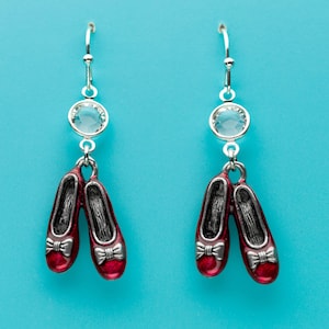 May include: A pair of silver earrings with red ruby slipper charms and clear crystal accents.