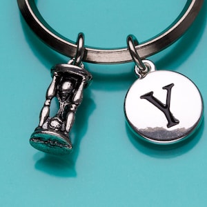 May include: Silver keyring with a small hourglass charm and a round charm with the letter Y in black.