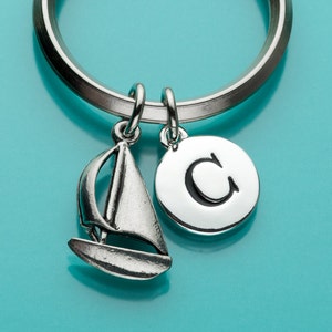 May include: Silver keychain with a sailboat charm and a round charm with the letter "C" in black lettering.