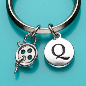 May include: Silver keychain with a silver button charm and a silver charm with the letter Q on it.