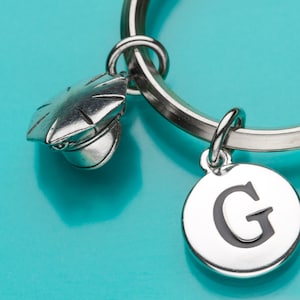 Può includere: Portachiavi d'argento con un ciondolo d'argento a forma di cappello da poliziotto e un ciondolo d'argento con la lettera G.