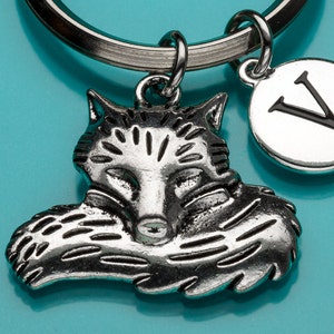 May include: Silver fox keychain with a silver charm with the letter V on a blue background.