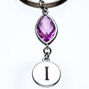 May include: A silver keychain with a purple crystal charm and a silver charm with the letter I.
