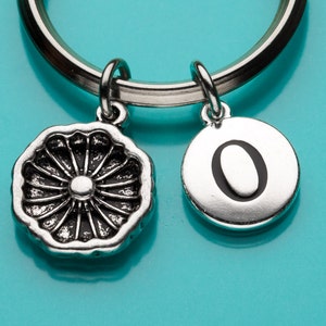 May include: A silver key chain with a decorative charm and a charm with the letter "O" on it.