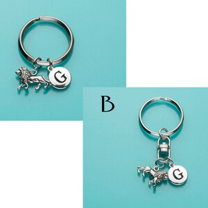May include: Two silver keychains with a lion and a unicorn charm. Both keychains have a silver letter G charm.