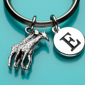 Puede incluir: Llavero de plata con dos dijes de jirafa de plata y un dije de plata con la letra E en negro.