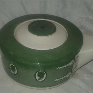 May include: A green and white teapot with a lid and a white handle. The teapot has a floral design with a silhouette of a woman in each flower.