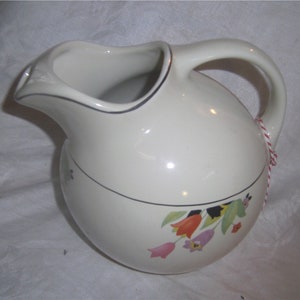 May include: White ceramic pitcher with a floral design featuring pink, orange, and purple tulips. The pitcher has a silver rim and a round body with a wide spout and a handle.