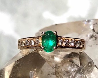 May include: A gold ring with a green emerald gemstone and a band of small diamonds.