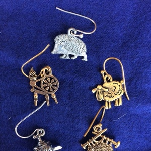 May include: Four pairs of silver and gold tone earrings with a variety of charms, including a hedgehog, a spinning wheel, a sheep, and a knitted sweater.