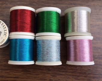 May include: Six spools of 601 Fine Metallic thread, each 100 meters long. The spools are in the colors red, green, silver, blue, light blue, and pink.