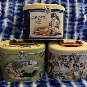 May include: Three vintage metal tins with lids. The tins are decorated with images of children and the text "J & P Coats Best Six Cord Threads".