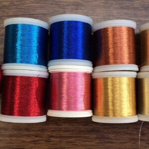 May include: Eight spools of metallic thread in various colors, including blue, red, gold, silver, and copper. The spools are labeled "Metallic Madera" and are made in Germany.