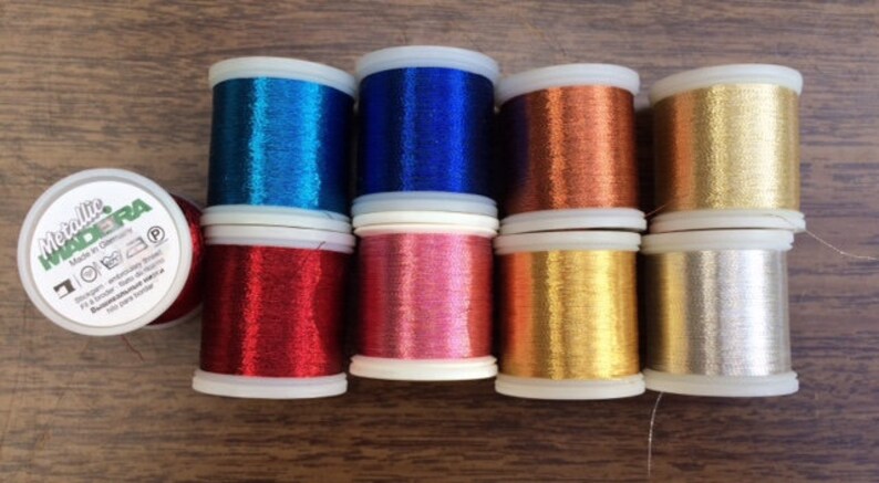 May include: Eight spools of metallic thread in various colors, including blue, red, gold, silver, and copper. The spools are labeled "Metallic Madera" and are made in Germany.