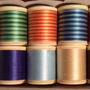 May include: Ten spools of thread in various colors and patterns, including red, green, blue, orange, and brown. The spools are arranged in two rows of five.
