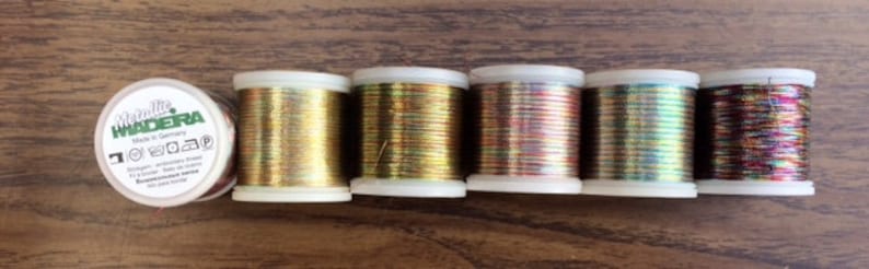 May include: Six spools of iridescent metallic thread in gold, red, green, blue, and purple. The spools are labeled "Made in Germany" and "Madeira".