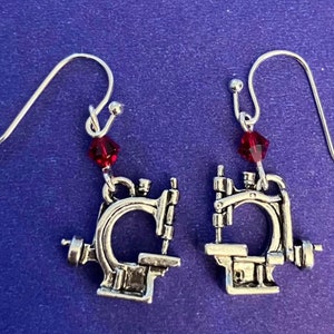 May include: A pair of silver earrings featuring a miniature sewing machine charm with a red crystal dangle.