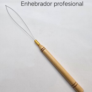 Puede incluir: Un enhebrador de aguja de madera con una punta de metal dorado y un fino bucle de alambre en el extremo. El enhebrador está etiquetado como "Enhebrador profesional".