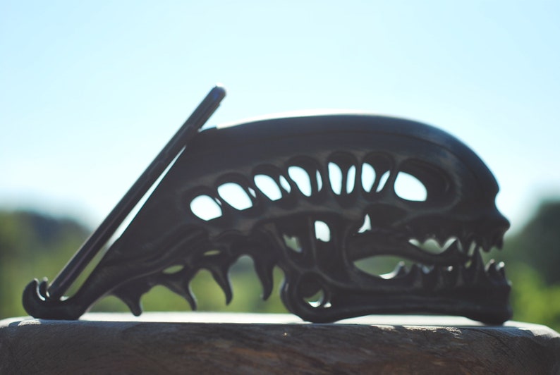 May include: A black phone stand shaped like an alien skull with a phone propped up against it.