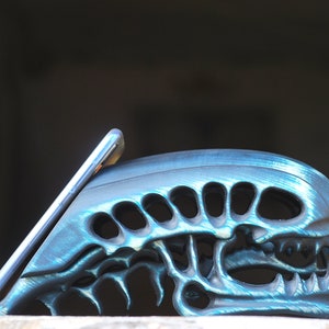 May include: A teal blue phone stand shaped like an alien head with a phone resting in the stand.