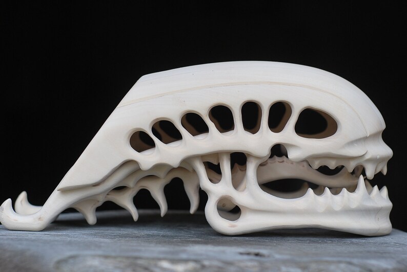 May include: A white, detailed, carved sculpture of an alien skull. The skull is open and shows the intricate details of the inside of the skull.