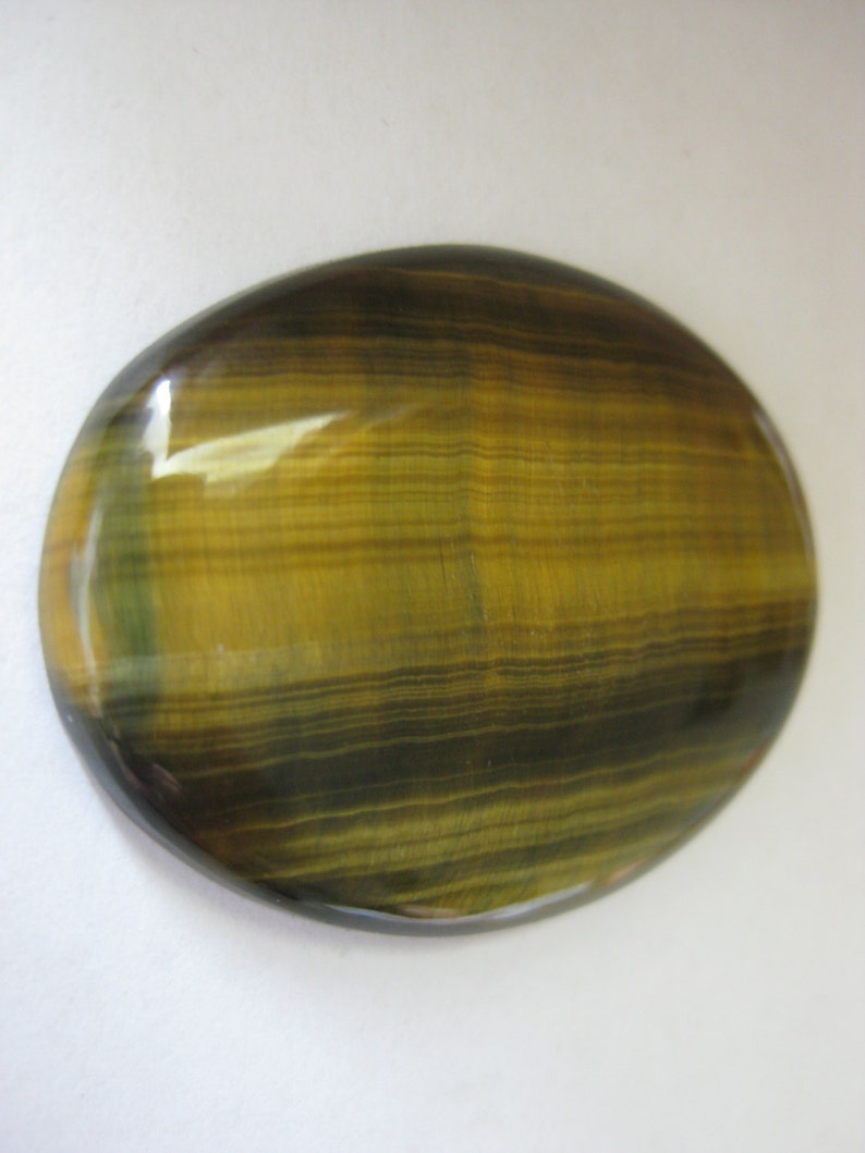 May include: A smooth, oval-shaped tiger's eye gemstone with a golden brown and black striped pattern.