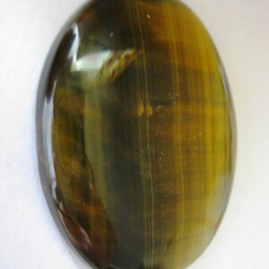 May include: A smooth, oval-shaped tiger's eye gemstone with a golden brown and black colour pattern.