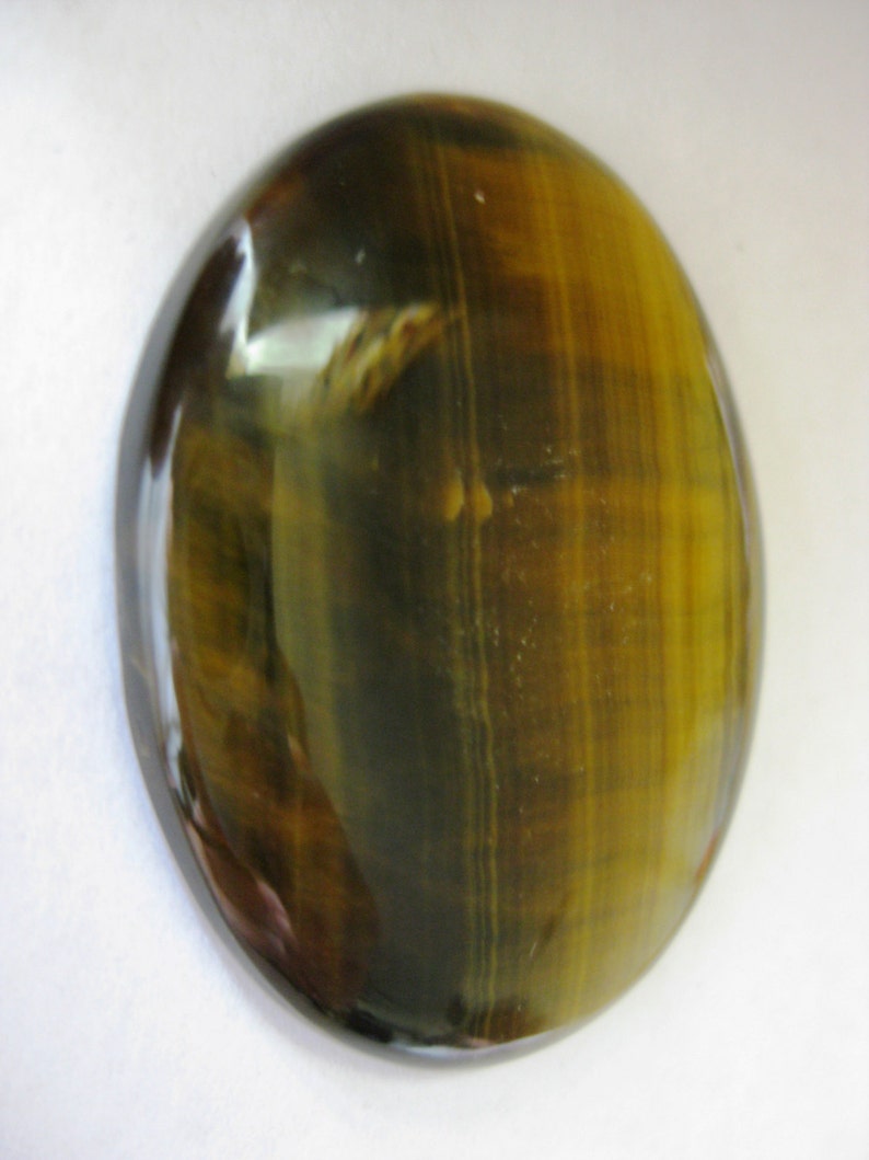May include: A smooth, oval-shaped tiger's eye gemstone with a golden brown and black colour pattern.