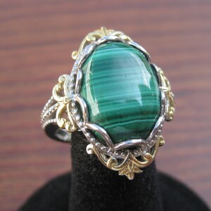 May include: A silver ring with a green malachite stone set in a gold and silver filigree design.