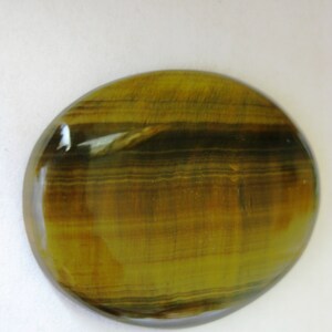 May include: A smooth, oval-shaped tiger's eye gemstone with a golden brown and black striped pattern.