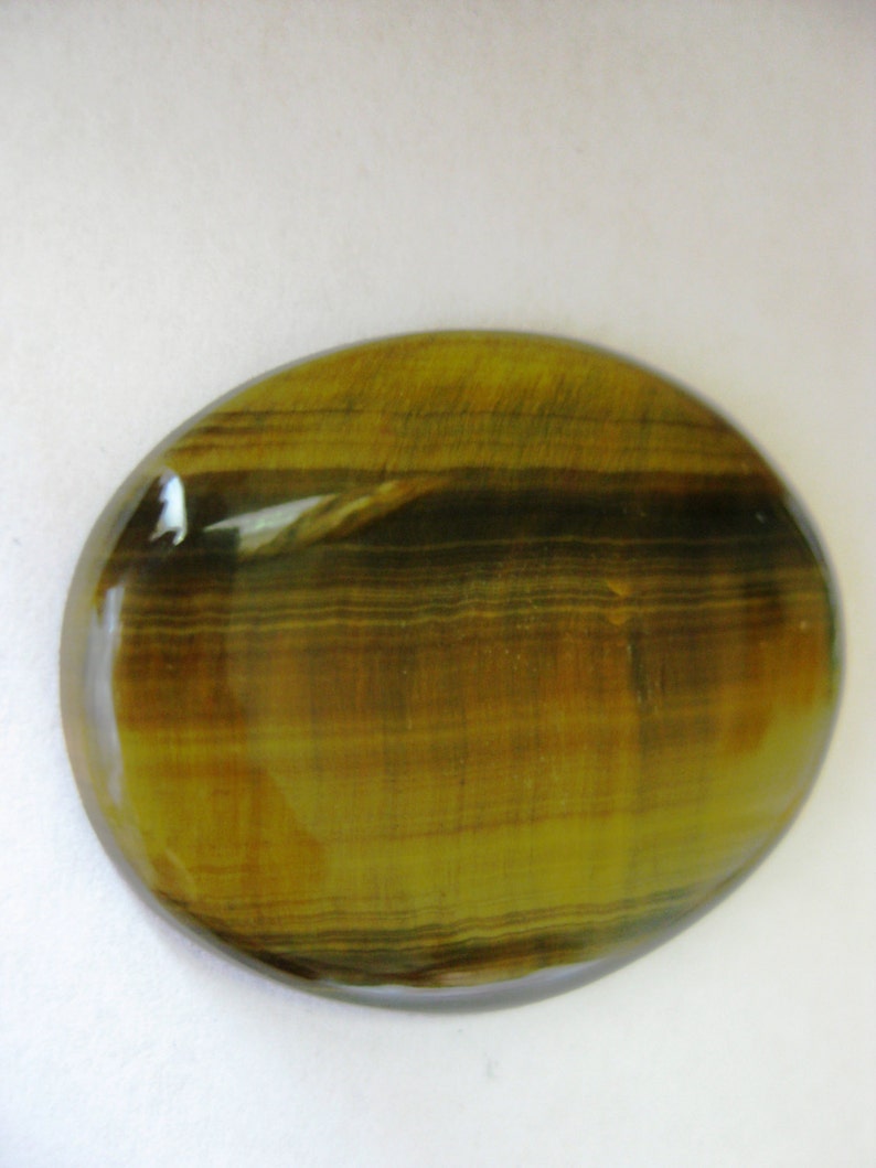 May include: A smooth, oval-shaped tiger's eye gemstone with a golden brown and black striped pattern.