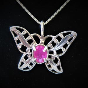 May include: A silver butterfly pendant necklace with a pink gemstone in the center.