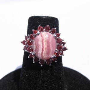 May include: A silver ring with a pink and white striped oval gemstone surrounded by a halo of red gemstones.