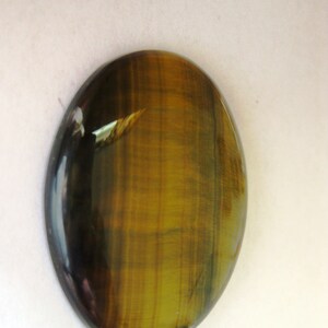 May include: A smooth, oval-shaped tiger's eye gemstone with a golden brown and black colour pattern.