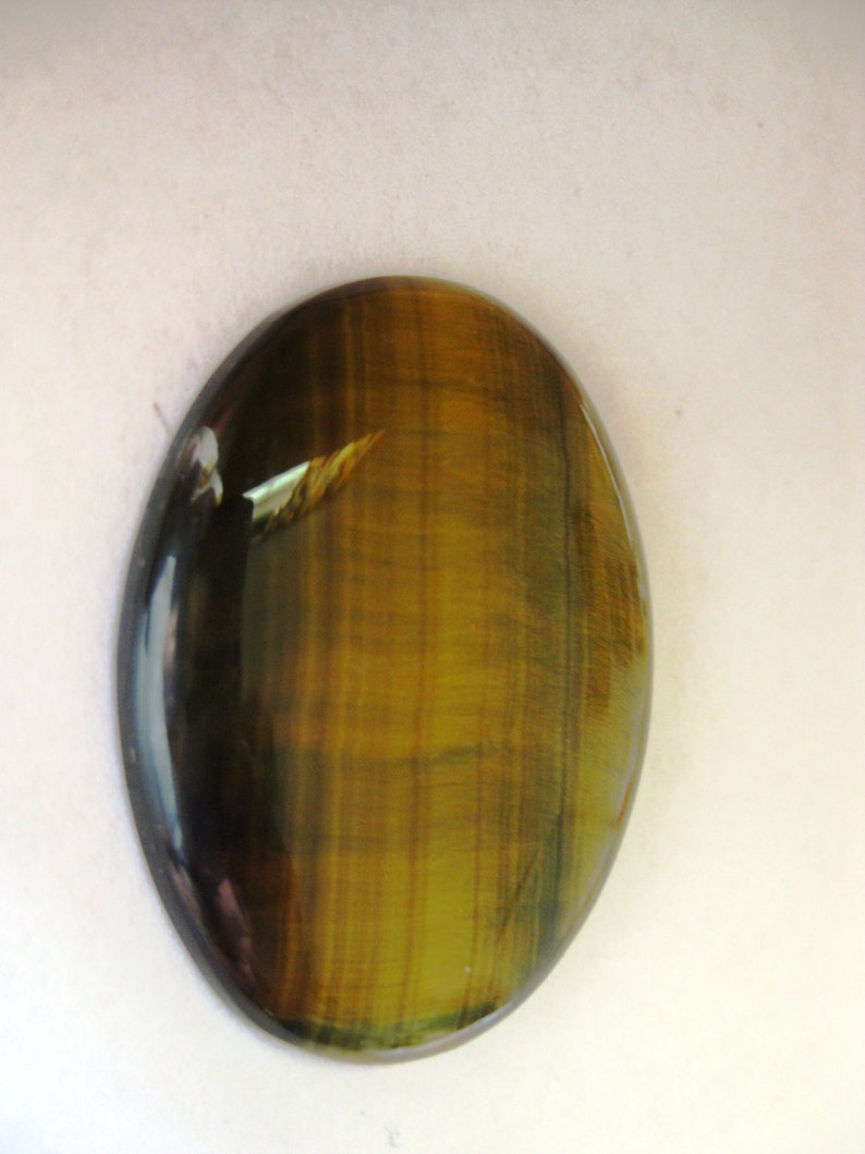 May include: A smooth, oval-shaped tiger's eye gemstone with a golden brown and black colour pattern.