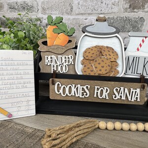 May include: A Christmas-themed wooden display featuring a note to Santa, carrots, cookies, and milk. The note reads "Dear Santa, I have been extra good this year..." with the words "REINDEER FOOD" and "COOKIES FOR SANTA".