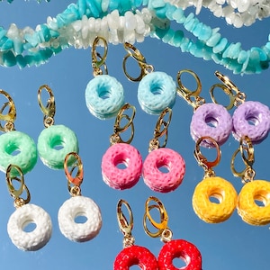 May include: Assortment of colorful donut-shaped earrings with gold hoops. The earrings are made of plastic and come in a variety of colors, including pink, blue, green, white, and yellow.