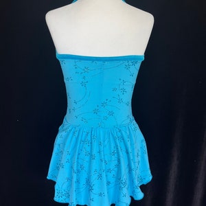 May include: A light blue figure skating dress with a halter neckline and a floral pattern. The dress has a ruffled skirt and a velvet trim.